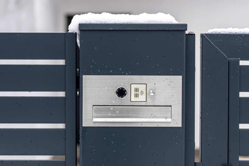 Eine moderne Video Türsprechanlage an einem Briefkasten, montiert in einem Paneelzaun in anthrazitfarbener Farbe