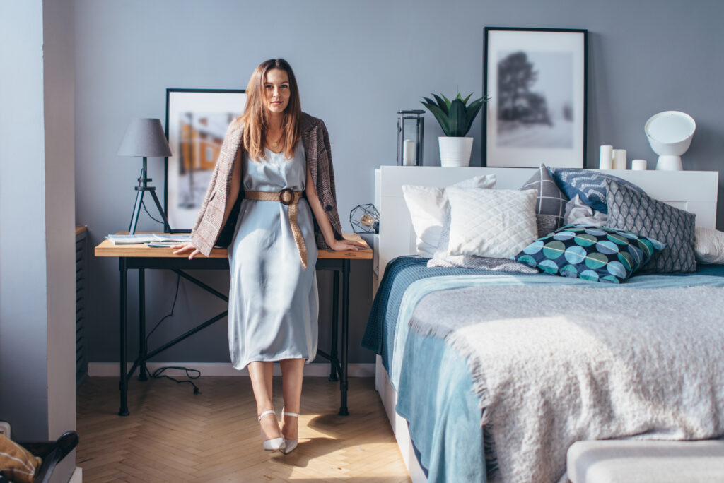 Moderne Frau steht vor einem stilvoll eingerichteten Schlafzimmer mit geschichtetem Bett und spannbettlaken 200x200 – Kombination aus Interior-Design und Schlafqualitaet
