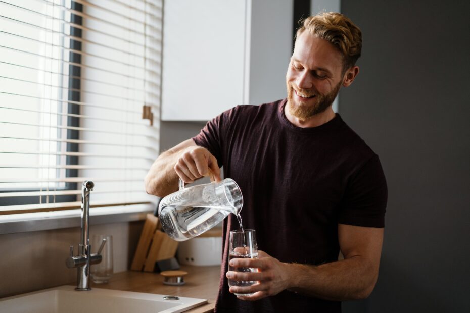 Mann giesst Wasser aus Karaffe in Glas | Wasserspender für zuhause